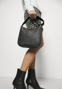 Sort læderhåndtaske med struktureret overflade, der har en buet top, kort håndtag og sølvfarvede hardware-detaljer.