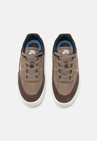 Nike SB tenisice, sa smešnom suđenom i tekstilnom gornjom površinom, ljubičastim vezicama, belim međuslojem i plavim unutrašnjim oblogama. Klasičan dizajn tenisica za skejtanje.