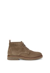 Bottines en daim marron avec six œillets et des lacets beiges, présentant un bout rond et une semelle en caoutchouc texturée avec un léger talon.