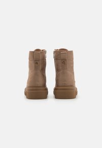 Bottines en suède marron avec une texture lisse, fermeture zippée et une semelle en caoutchouc robuste. Comprend un petit détail de logo et une pointe arrondie.