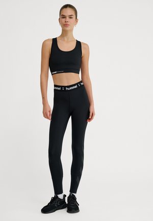 Black sports bra with a logo band, paired with high-waisted black leggings featuring a diagonal stripe pattern and black athletic shoes.