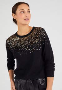Maglione nero con scollo rotondo e maniche a tre quarti, decorato con paillettes dorate in un motivo gradiente lungo il colletto.
