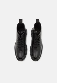 Paire de bottines en cuir noir brillant avec lacets et fermetures éclair latérales, vues de dessus sur un fond blanc uni.