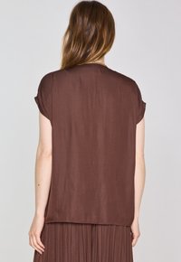 Top corto marrone a maniche corte con vestibilità rilassata, realizzato in tessuto liscio, caratterizzato da un collo rotondo e dettagli di cucitura minimi all'orlo.