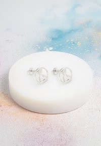 Silverfärgade studörhängen med en cirkulär design som har ett hjärtformat utskärning i mitten, visade på en vit rund yta.