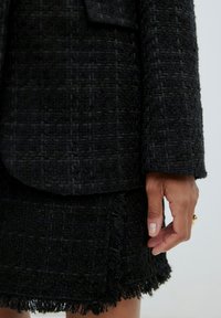 Zwarte tweed blazer met een gestructureerde afwerking en franjes op de onderrand van de rok, met subtiele patronen en een ontspannen, gestructureerde pasvorm.