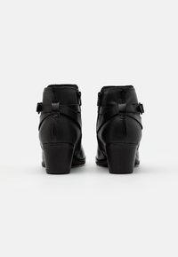 Czarne botki za kostkę o fakturowanym wykończeniu, zapinane na zamek, z krzyżującymi się paskami. Posiadają średni obcas i gładkie, wypolerowane akcenty.