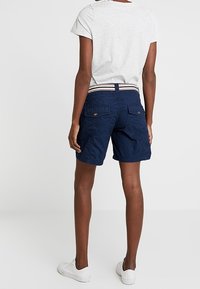 Shorts cargo azul marino con una tela texturizada, cintura elástica con rayas blancas y dos bolsillos traseros. Combinados con una camiseta gris.