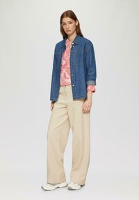 Een spijkerjack over een rood-wit gestreepte blouse, gecombineerd met beige wijde broek en lichtgrijze sneakers. Eenvoudige, casual outfit.