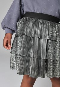 Jupe noire en couches fabriquée dans un matériau plissé brillant. Elle possède une taille lisse et une finition texturée irisée.