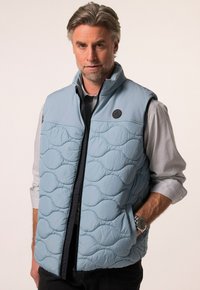 Svetle modrá prošívaná vesta s vysokým límcem, zapínáním na zip a bočními kapsami. Disponuje texturovaným vzorem a kruhovým logem značky na hrudi.