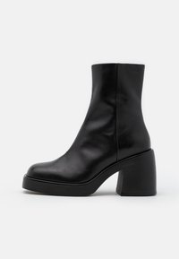 Bottines en cuir noir avec un bout arrondi et un talon épais et haut. Texture lisse avec un design minimaliste et sans quincaillerie visible.