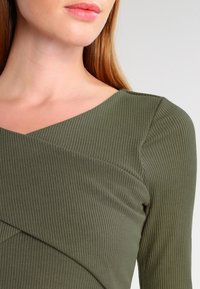 Olivově zelený žebrovaný dlouhý rukáv top s překříženým výstřihem do V, s jemnou texturou a přiléhavým střihem.