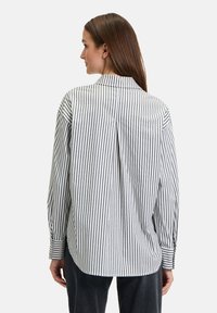 Gestreiftes Langarmhemd in Schwarz und Weiß, mit lockerer Passform, Knopfmanschetten und einem Faltenwurf hinten für zusätzliche Beweglichkeit.