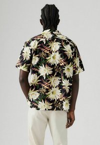 Camisa de flores de manga corta en negro, con grandes flores blancas y amarillas y hojas verdes. Tejido ligero con un ajuste relajado.