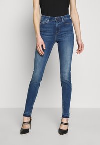 Tajta blå denimjeans med midjehöjd, subtil blekning och fem fickor, tillsammans med svarta sandaletter med hög klack.
