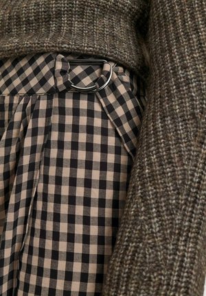 Maglione lavorato a maglia in tonalità terrose accanto a una gonna plissettata con motivo a quadretti neri e beige, caratterizzata da un dettaglio con fibbia in metallo circolare.