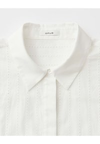 Weißes Hemd mit Knopfleiste, spitzem Kragen und vertikalen Ösen-Spitzen-Details, Markenlabel "OPUS" innen am Kragen.