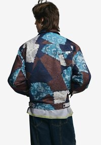 Kurtka patchworkowa wykonana z niebieskich, brązowych i białych tkanin o różnych wzorach. Posiada zapięcie na guziki oraz metkę na plecach.