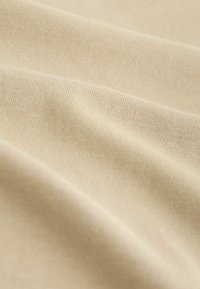 Gros plan d’un tissu beige lisse avec une texture côtelée fine et des plis doux.