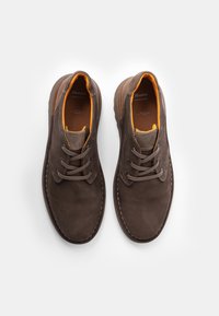 Zapatos de cuero marrón con un acabado texturizado, punta redonda y un forro interno naranja en contraste. Presentan cordones y detalles de costura sutiles.