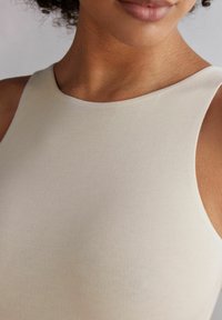 Beige ärmlös topp med en mjuk, elastisk textur; har en rundad halsringning och rena linjer som betonar en åtsittande design.