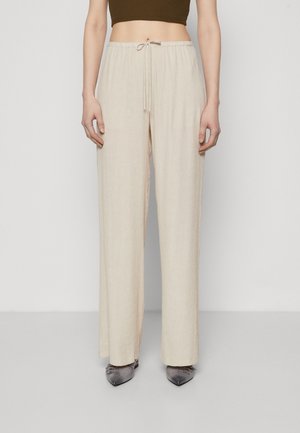 Pantalons large beige clair en tissu texturé, dotés d'une taille élastique et d'une coupe décontractée. Assortis à des chaussures grises à bouts pointus.