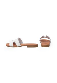 Hvide flade sandaler med åben tå, der har to brede stropper. Sålen er brun, lavet af et læderlignende materiale, med et enkelt design.