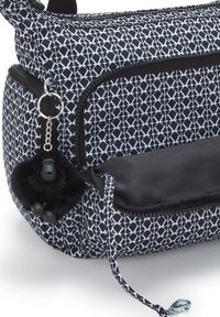 Black and white patterned bag with a zippered closure, featuring a faux fur keychain and black accents on the bottom and zipper.