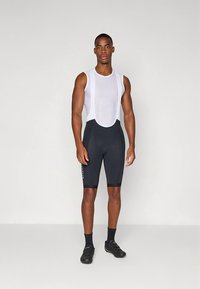 Biciklistička odjeća koja se sastoji od bijelog, mrežastog topa bez rukava i crnih kratkih hlača uskog kroja s crnim detaljima i diskretnim brendiranjem sa strane.