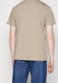 Beige bomulds-T-shirt med korte ærmer, en rund halsudskæring og en afslappet pasform, vist bagfra med en glat tekstur.