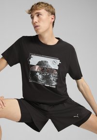 Sort bomulds T-shirt med grafisk design med bjerge og bølgede mønstre i grå og rød. Bæres med sorte shorts, blød tekstur.