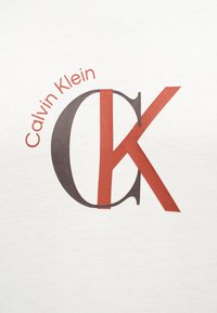 Το λογότυπο της Calvin Klein με ένα μεγάλο μαύρο "C" και κόκκινο "K" που επικαλύπτονται, και το κείμενο "Calvin Klein" κυρτό από πάνω σε κόκκινο χρώμα σε λευκό φόντο.