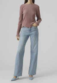 Faltiges Langarm-Top in Mauve, kombiniert mit hoch taillierten, hellblauen Weitbein-Jeans und grauen, spitzen Absatzschuhen, vor einem neutralen Hintergrund.
