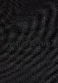 Čierna textília s tkanou textúrou a embosovaným logom "9N H'M SENSE". Materiál je hladký a vystihuje jemné vzory.
