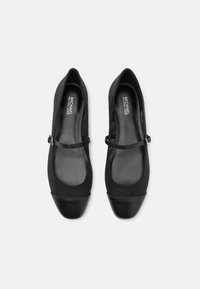 Black flats with a rounded toe, featuring a sleek design, matte texture, and a strap across the instep. Made of synthetic material.