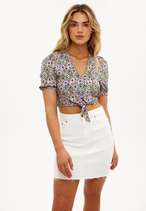 Femme portant un haut court à manches courtes lilas avec imprimé floral, noué à la taille, et une jupe en denim blanc taille haute avec ourlet effiloché.