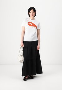 T-shirt branco com uma estampa de lagosta vermelha, emparelhado com uma saia maxi preta em camadas. Inclui uma bolsa branca e sapatos pretos tipo slip-on.