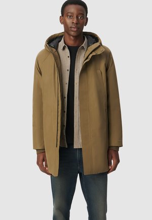 Oliwkowa, wodoodporna kurtka z kapturem, z zamkiem błyskawicznym i bocznymi kieszeniami, noszona na koszuli w kratę i ciemnych dżinsach.
