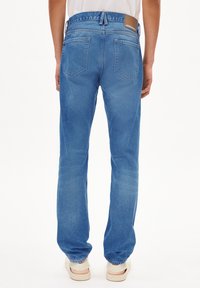 Jean en denim bleu avec une coupe droite, comprenant deux poches arrière, une étiquette de marque en cuir sur la ceinture, et une finition délavée.