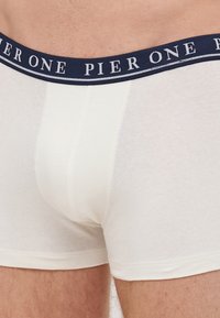 Fehér pamut boxer alsónadrág, navy kék rugalmas derékszallaggal, rajta a "PIER ONE" felirattal. Simaság jellemzi, és testhezálló kialakítása kényelmet biztosít.