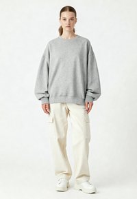 Felpa grigia oversize con scollo tondo e polsini a costine, abbinata a pantaloni cargo color crema con tasche laterali e sneakers bianche.