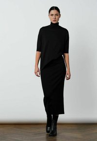 Sort langærmet turtleneck kjole med løstsiddende pasform, der har en lige silhuet og længde til midt på læggen. Bæres med sorte ankelstøvler.