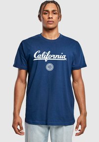 Námorně modré bavlněné tričko s bílým nápisem "California" a kulatým emblémem. Krátké rukávy, kulatý výstřih, volný střih.