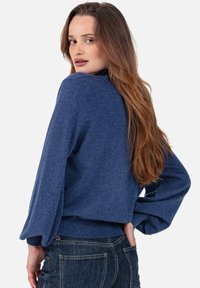 Pull bleu tricoté avec de longues manches bouffantes et un col arrondi. Présente des poignets et un ourlet côtelés, mettant en valeur une texture douce.