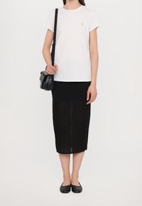 Bílý bavlněný tričko s malým logem, v kombinaci s černou pletenou midi sukni a černými plochými botami. Obsahuje malou černou crossbody kabelku.