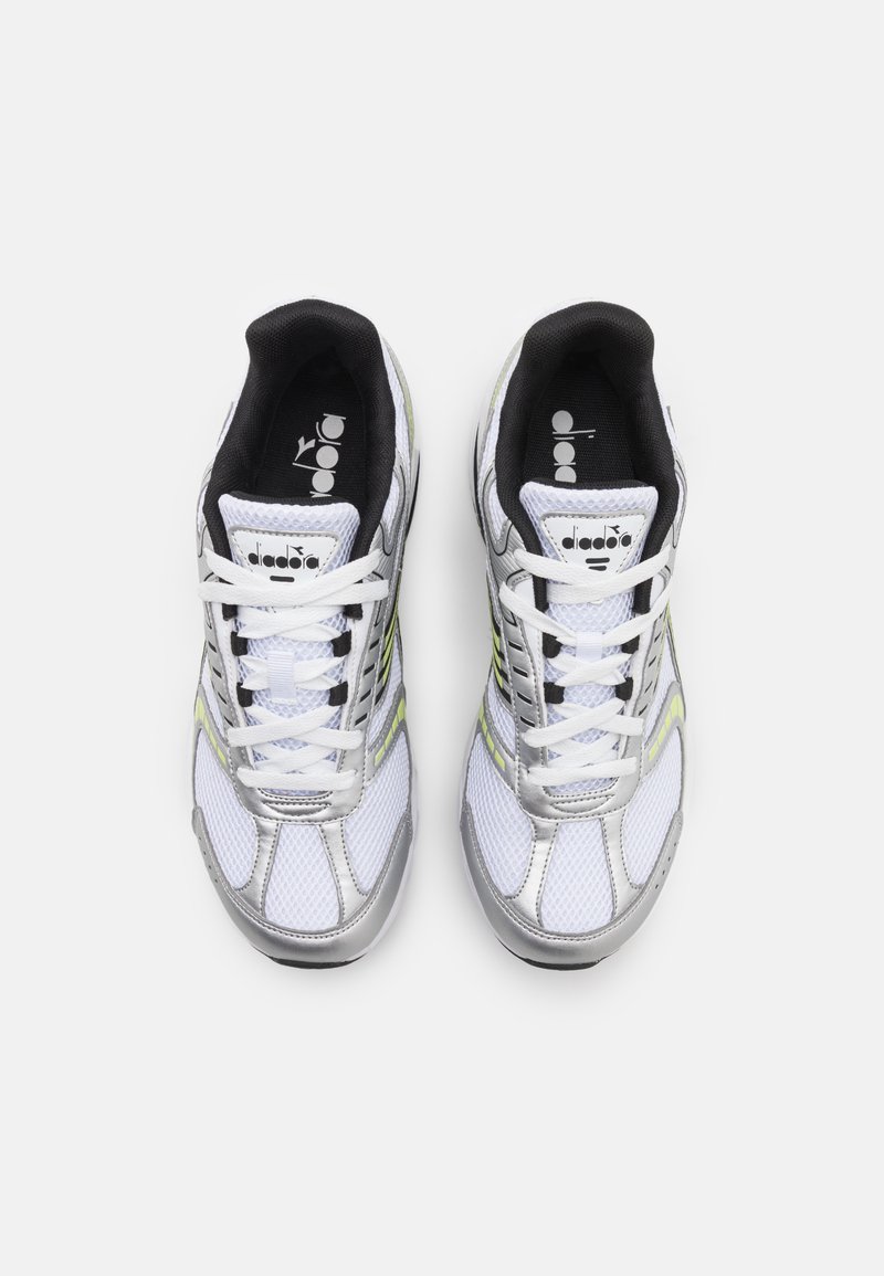Witte sportieve sneakers met mesh- en synthetische overlays, zilveren accenten, zwarte binnenvoering en fluorescent groene strepen aan de zijkanten.