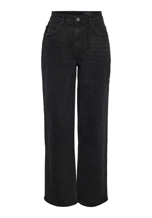 Person iført en hvid ærmeløs ribbet top, højtaljede sorte jeans og hvide sneakers med sorte striber, stående mod en ensfarvet baggrund.