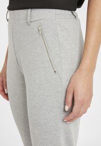 Pantalons de survêtement gris avec un tissu texturé, une taille élastique et une poche latérale zippée pour la fonctionnalité et le détail.