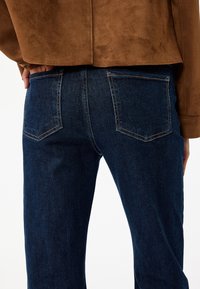 Vaqueros de denim azul oscuro con corte recto, que cuentan con dos bolsillos traseros con costuras decorativas y una textura sutil.